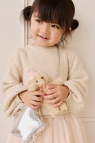Young girl holding a teddy bear and a silver bag against a white background