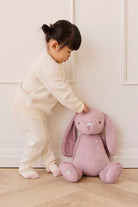 Child playing with a pink plush bunny toy against a white wall.