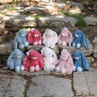 Plush bunnies in various colors sitting on stone steps outdoors.