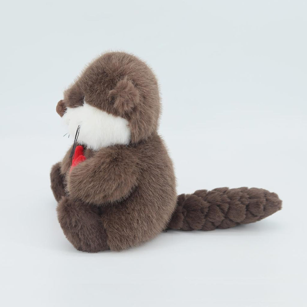 Plush toy otter holding a red heart on a light gray background