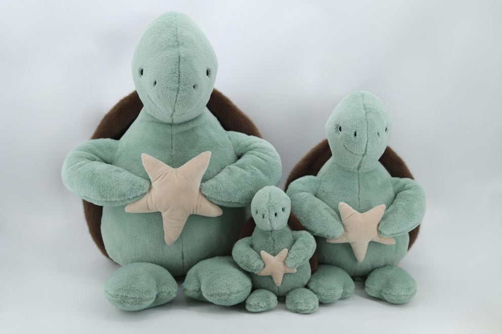 Set of three green plush turtles with star decorations on a white background