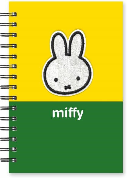 A spiral-bound notebook featuring a split yellow and green cover design, with a white glittery bunny face patch centered on the yellow section and the word 'miffy' in white on the green section.