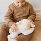 Child in a brown outfit holding a white Labmie plush toy on a light wooden floor.