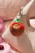 Plush keychain shaped like a character in a strawberry costume hanging from a handbag.