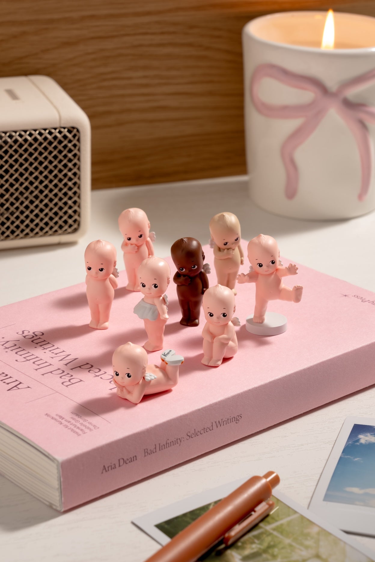 Small figurines of babies on a pink book with a candle in the background