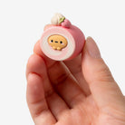 Small pink character figurine held in a hand against a white background