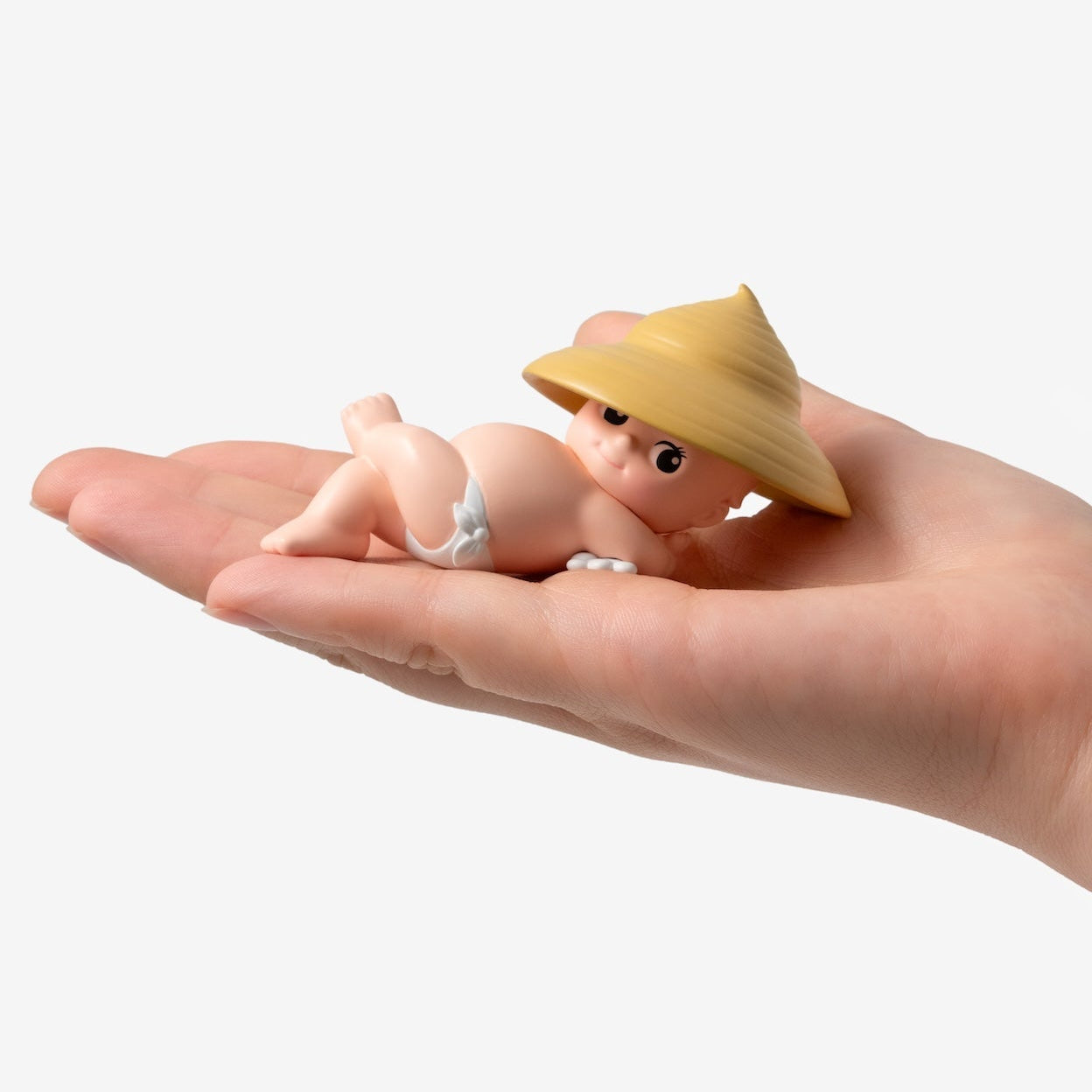 Small figurine of a baby wearing a straw hat held in a hand against a white background