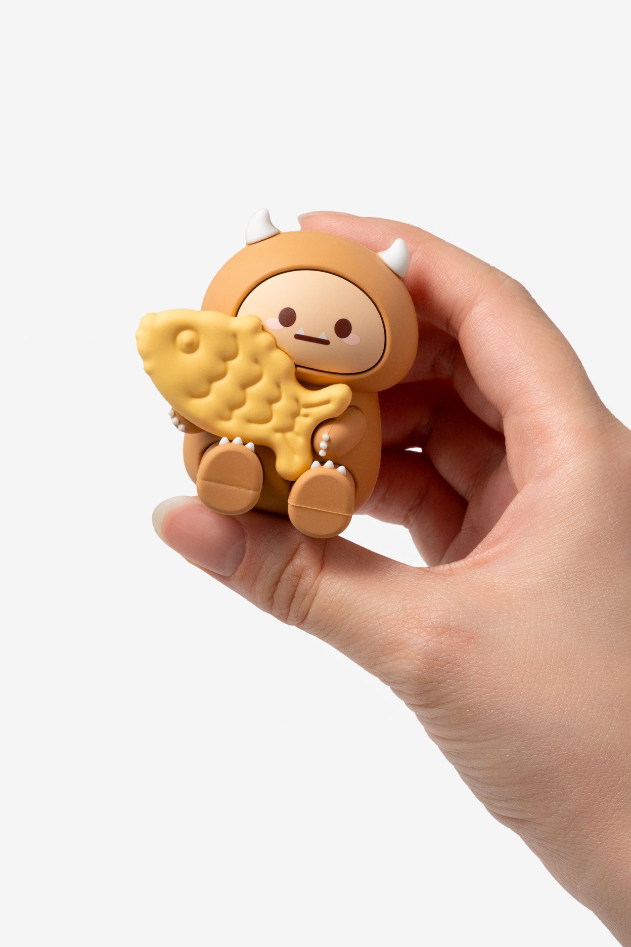 Hand holding a small, round, brown toy with a face and a yellow bear inside on a white background