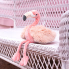 Plush flamingo toy on a wicker chair with a pink background