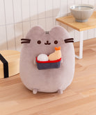 Plush toy shaped like a cat holding sushi on a wooden floor.