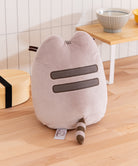 Plush cat-shaped pillow on a wooden floor with a blurred background