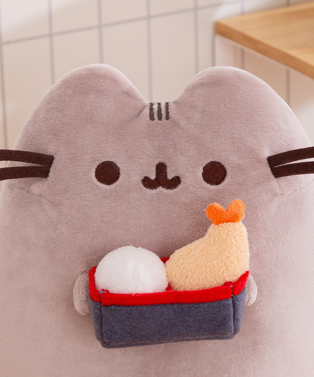 Plush toy resembling a cat with a small boat and fish on a neutral background