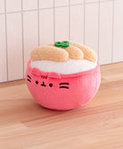 Plush toy shaped like a pink dumpling with a face on a wooden surface.