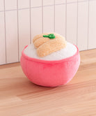 Plush toy resembling a peach with a pink base on a wooden surface.