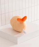 Plush toy resembling a peach with an orange top on a white surface.