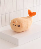 Plush toy resembling a cat with an orange tail on a white surface with a tiled wall background
