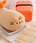 Plush toy shaped like a piece of bread with eyes and mouth on a white plate with an orange bento box in the background.