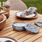 Candle in a decorative container on a wooden table with outdoor setting