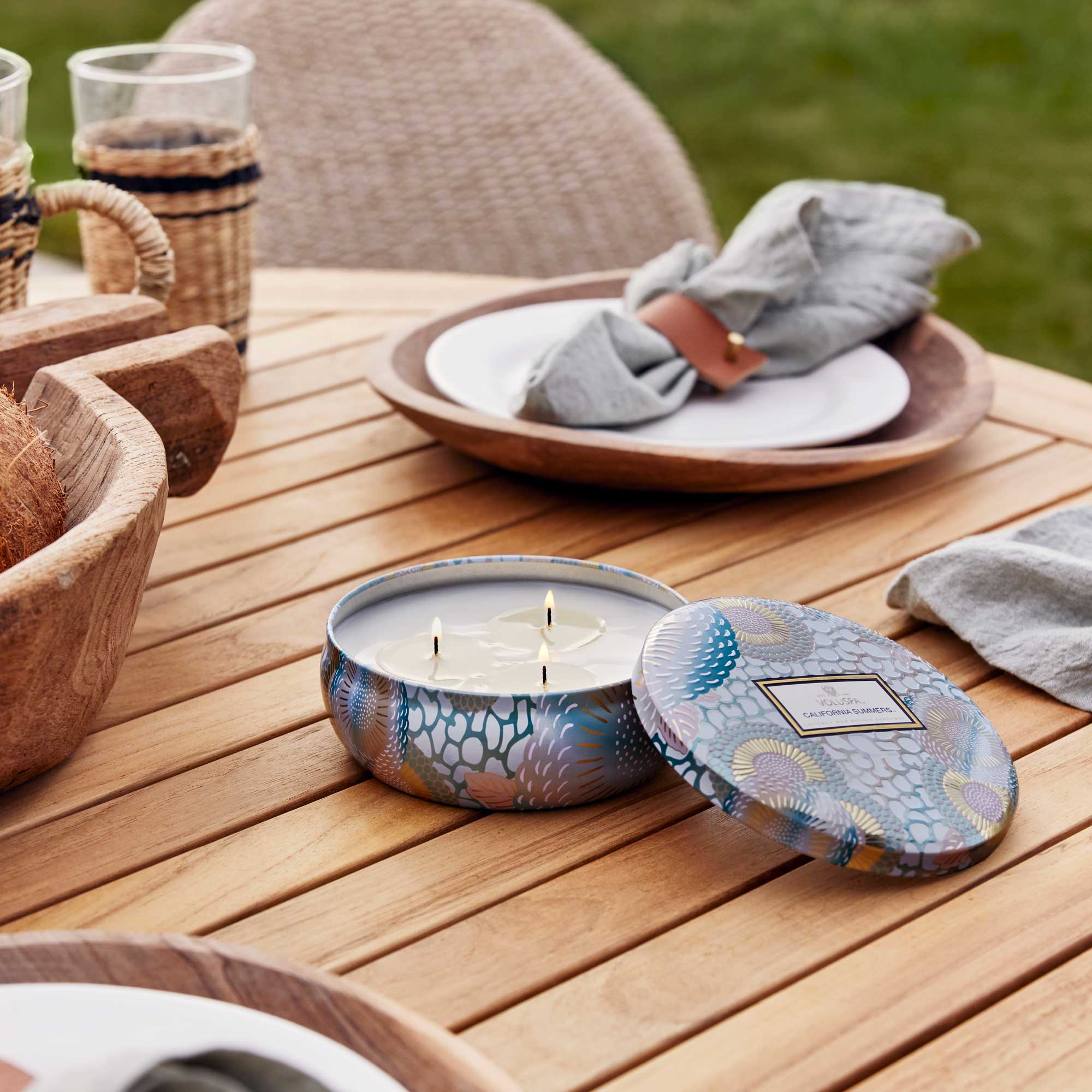 Candle in a decorative container on a wooden table with outdoor setting