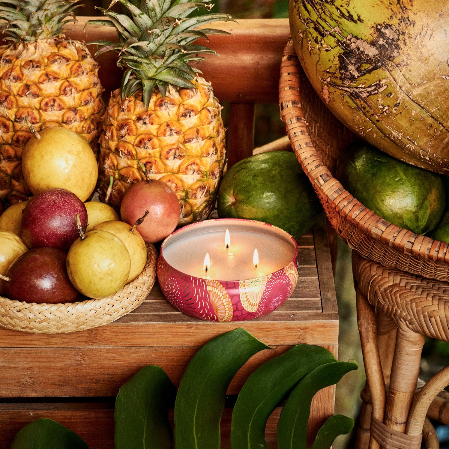 Fruit display with pineapples, apples, and a lit candle on a wooden surface.