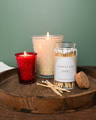 Candle, matches, and a container of matches on a wooden surface with a green background