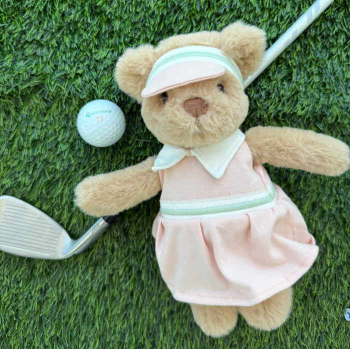Teddy bear in golf attire with a golf club and ball on grass