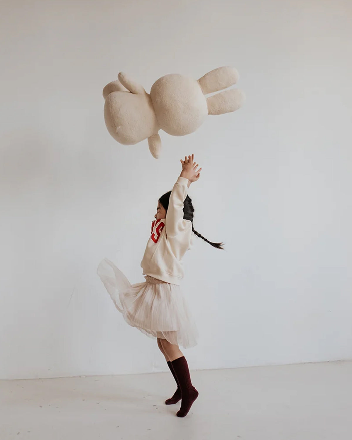 Person in a white sweater and skirt holding a large plush toy against a plain background