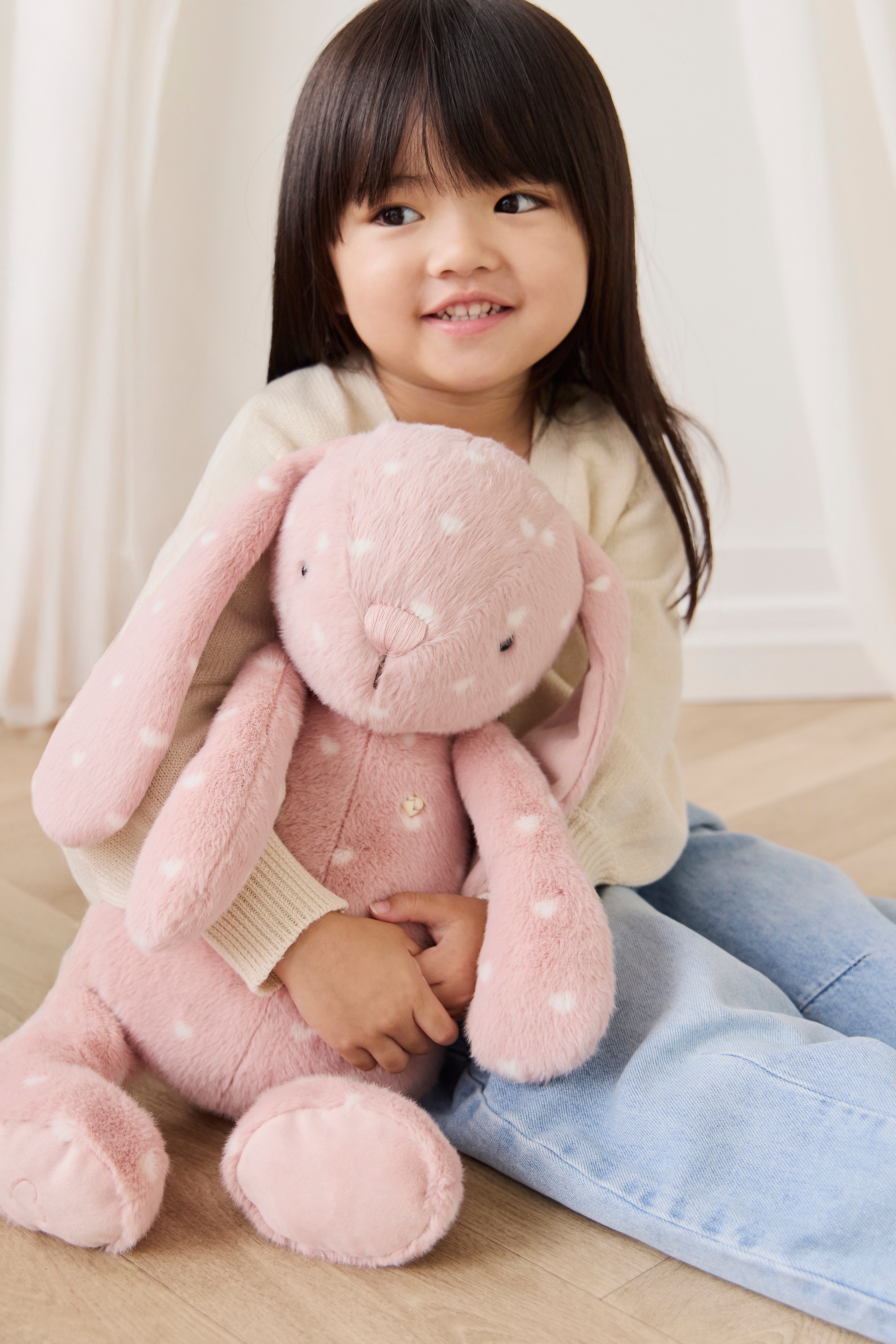 Child holding a pink plush bunny toy on a wooden floor.