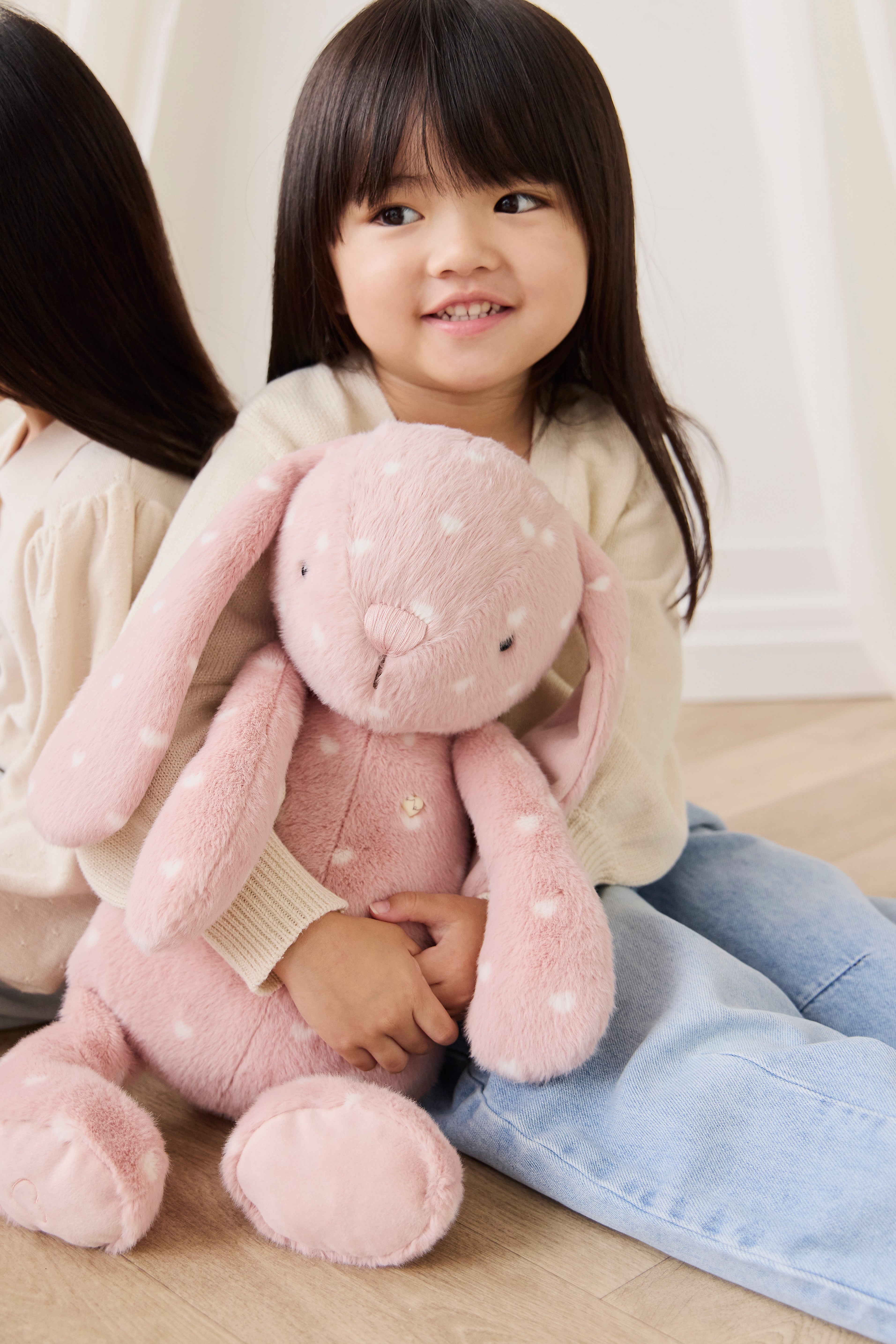 Child holding a pink plush bunny toy on a wooden floor.