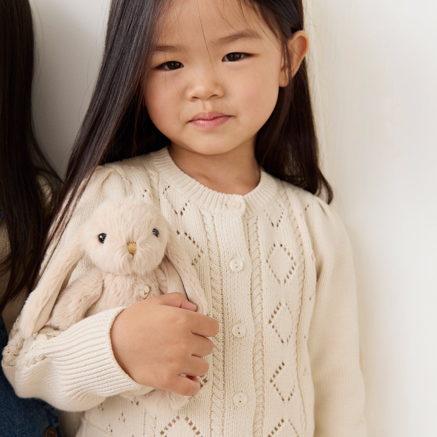 Young girl holding a plush bunny toy, wearing a cream sweater.