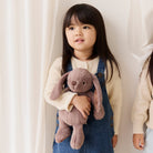 Child holding a plush bunny toy against a white curtain background