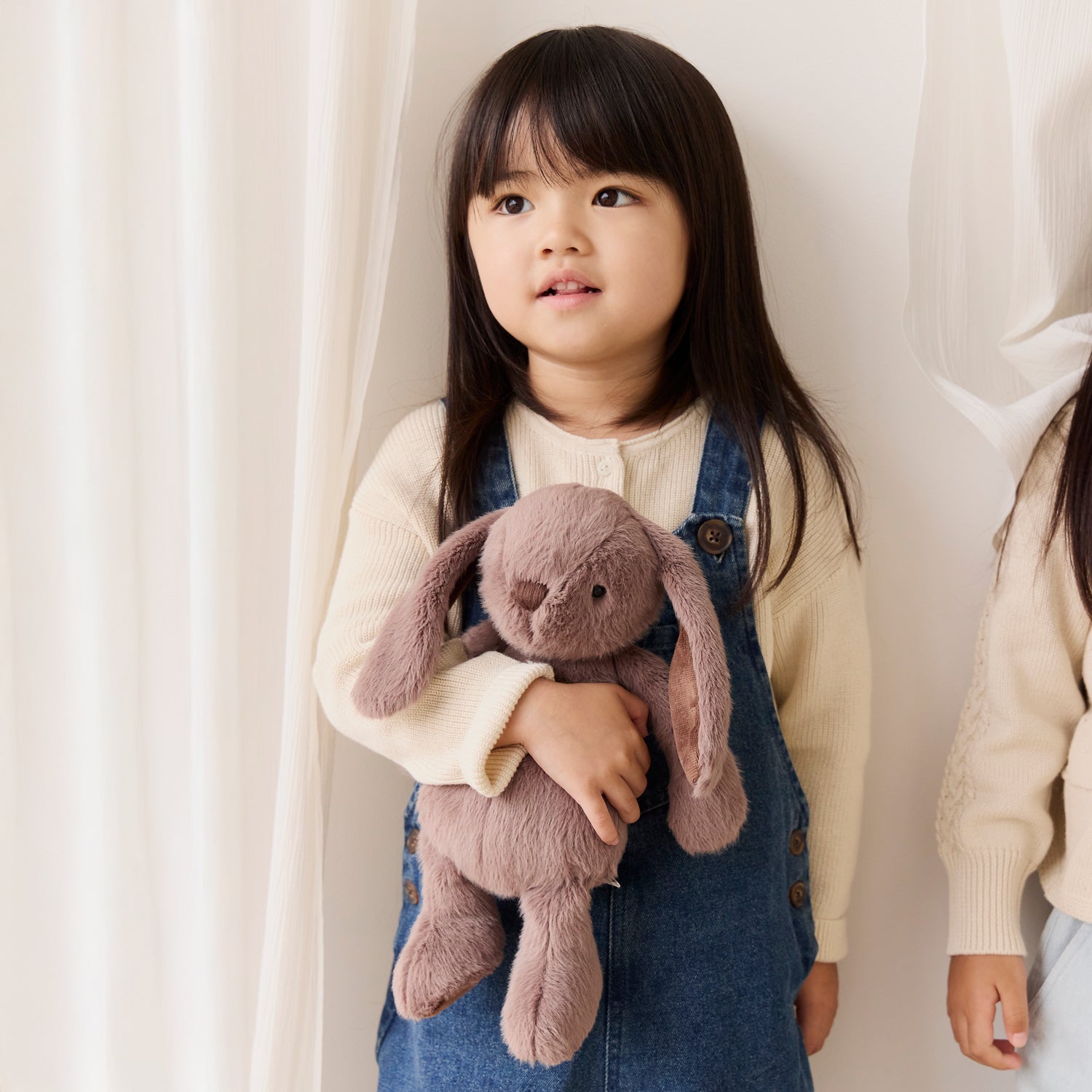 Child holding a plush bunny toy against a white curtain background