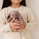 Child holding a plush rabbit toy wearing a beige sweater
