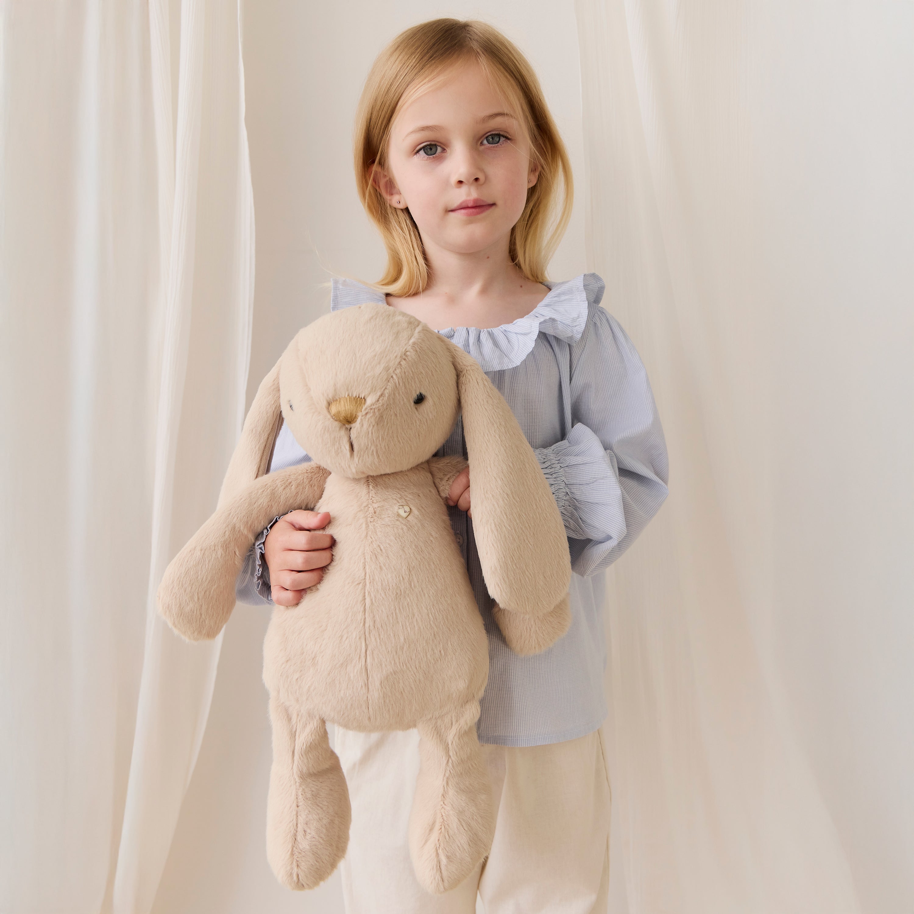 Young girl holding a beige stuffed bunny against a plain background