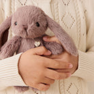 Person holding a plush bunny toy with a heart tag against a beige sweater background