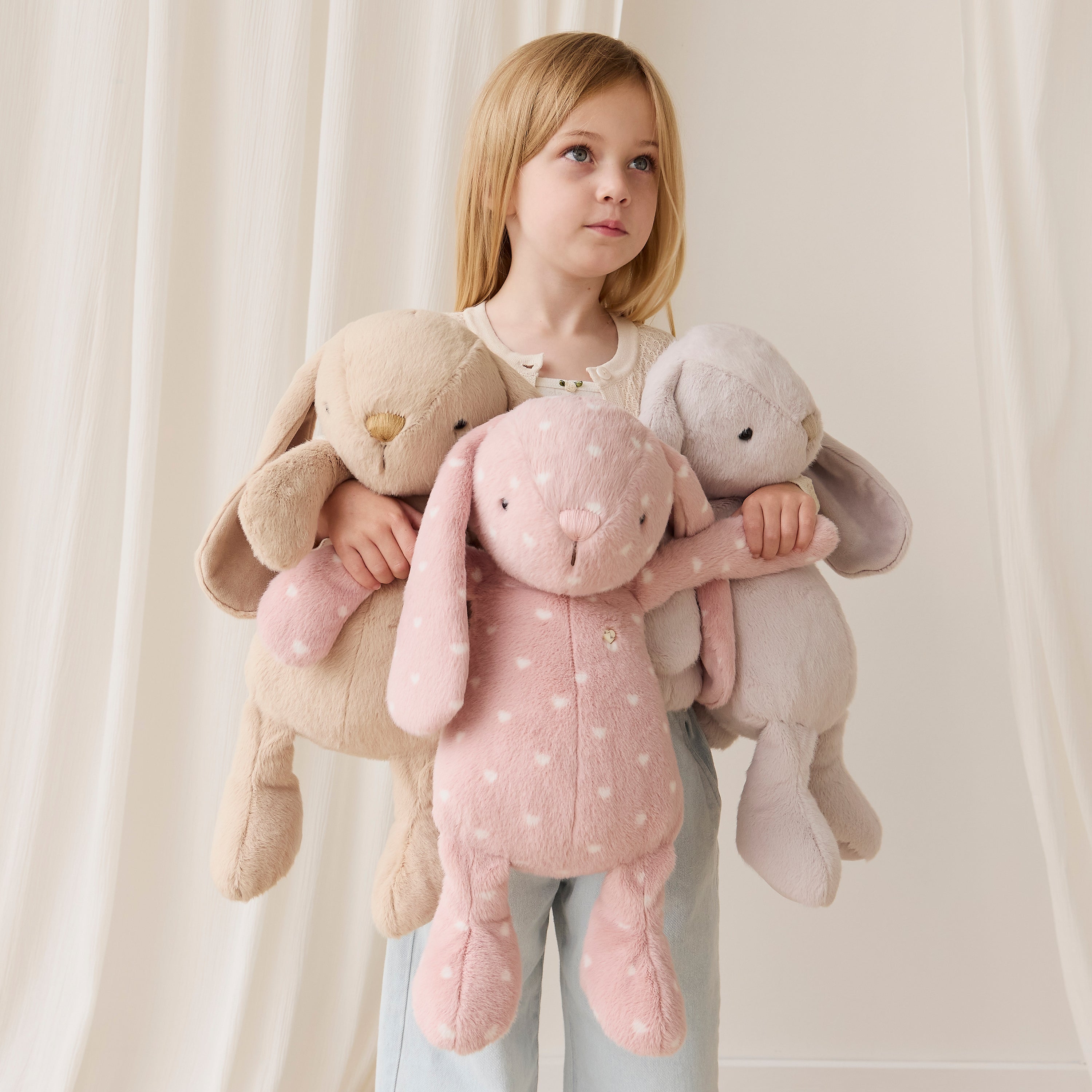 Child holding three plush toys against a plain background
