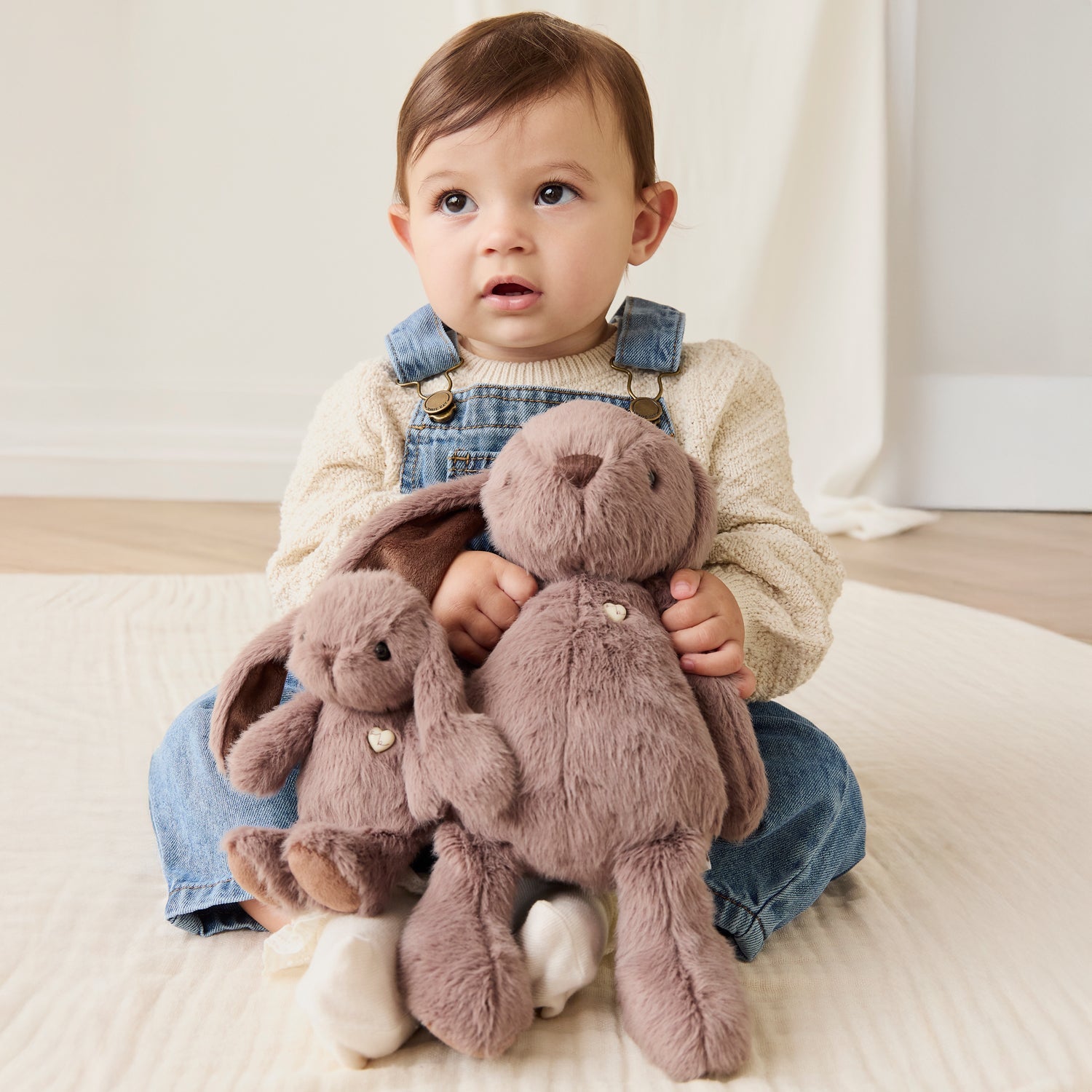 Child holding plush toys on a light-colored floor