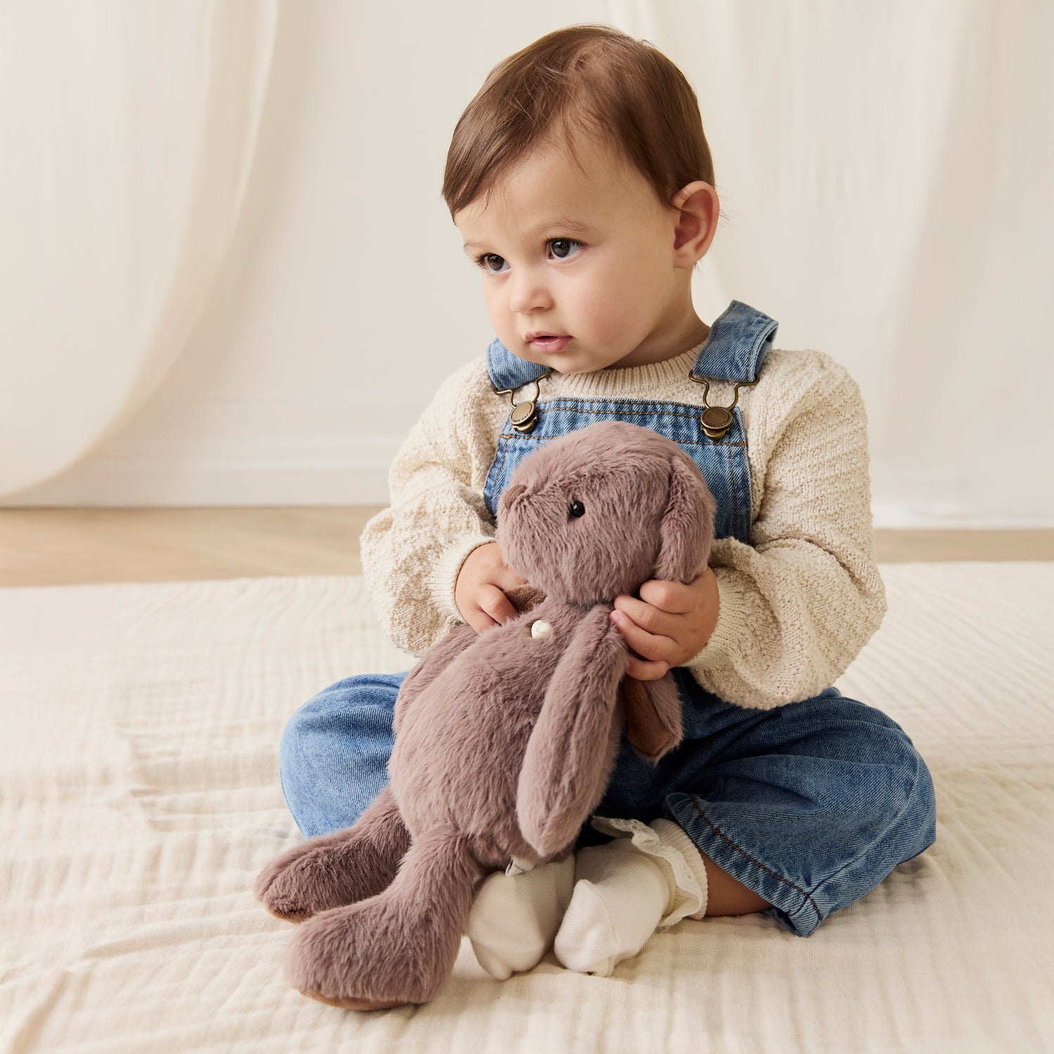 Baby holding a plush toy in a soft, neutral setting