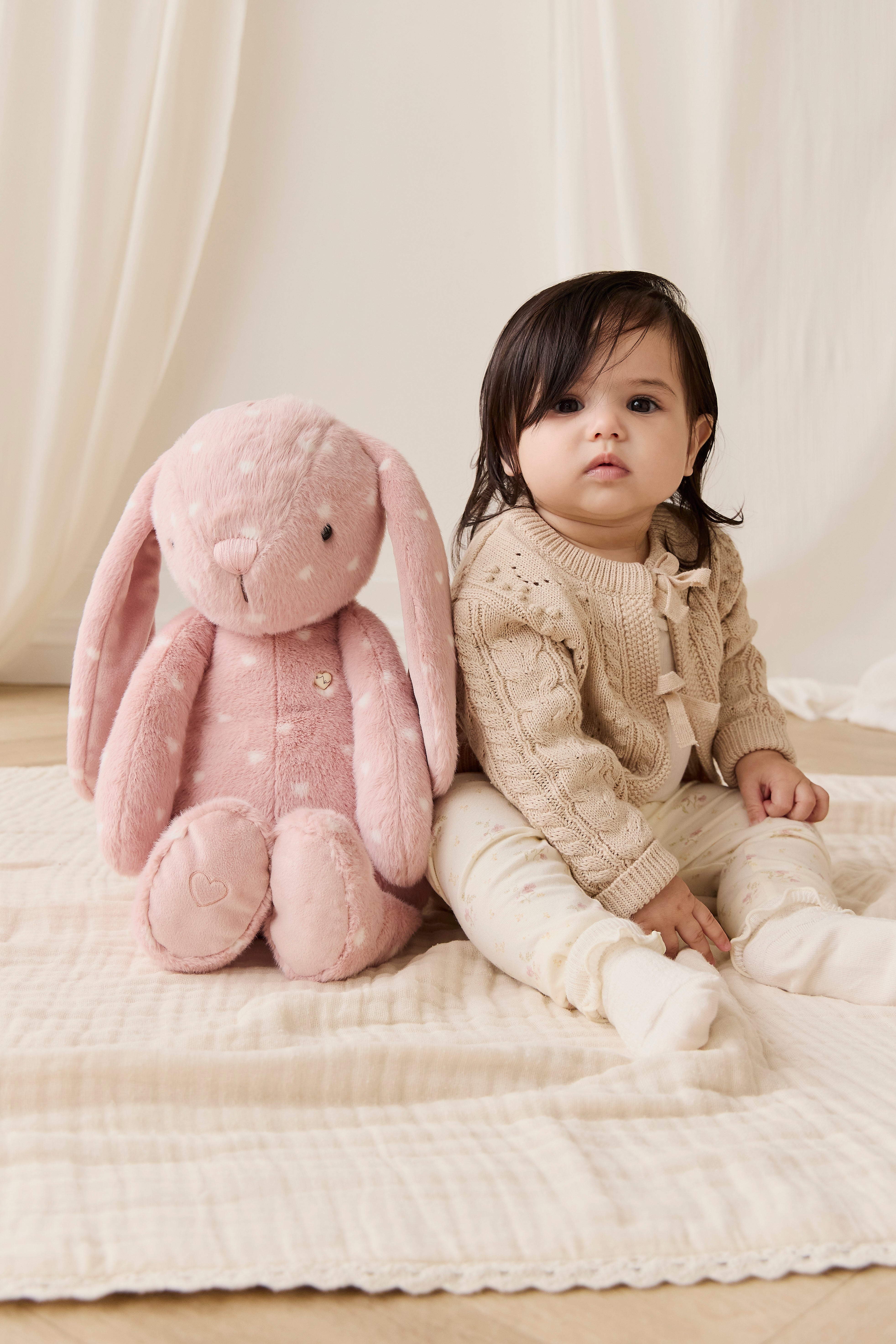 Child sitting on a bed with a large pink plush bunny toy