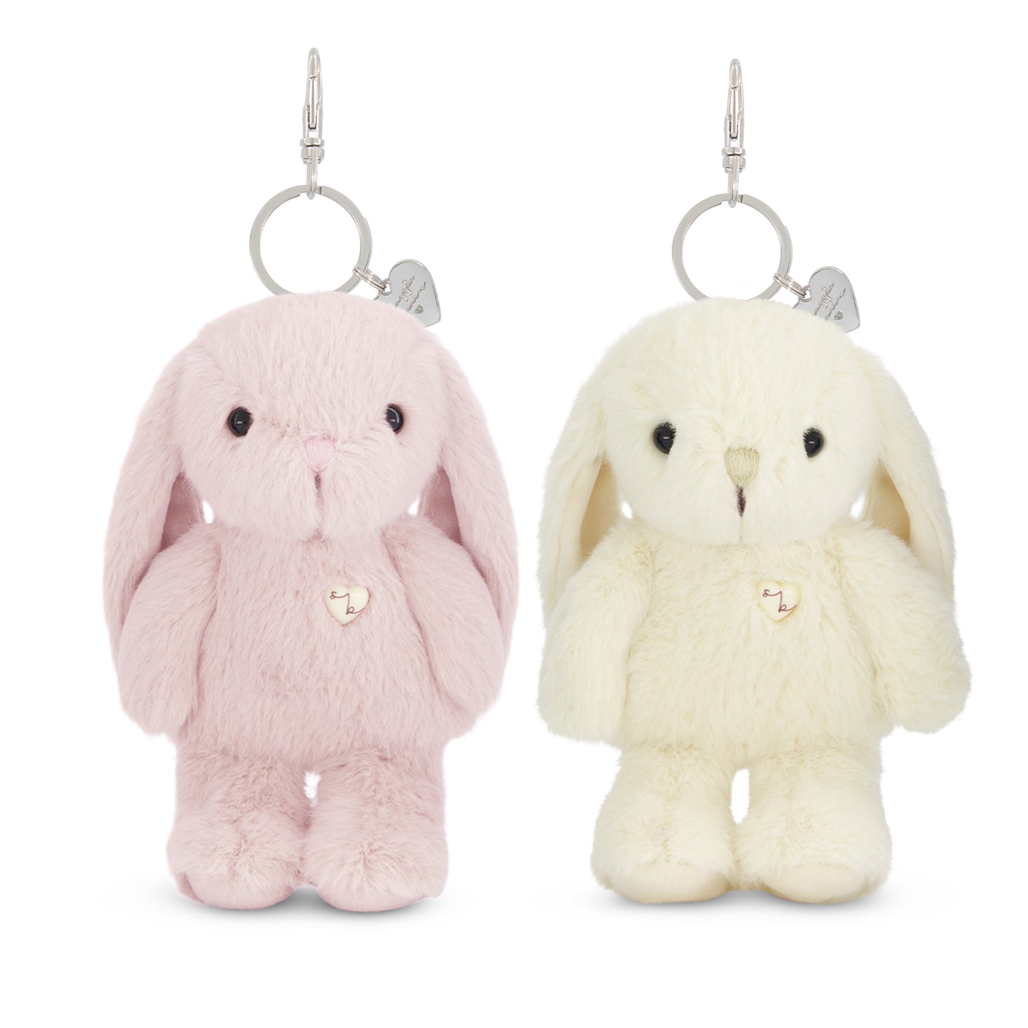 Two plush bunny keychains on a white background, one light pink and one cream/off-white, each with long floppy ears, small black eyes, a tiny stitched nose, and a small heart-shaped charm on a silver ring.