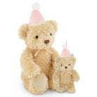 A beige teddy bear sits beside a smaller matching teddy bear ornament, both wearing pink party hats with white pom-poms and pink ribbons, on a white background.