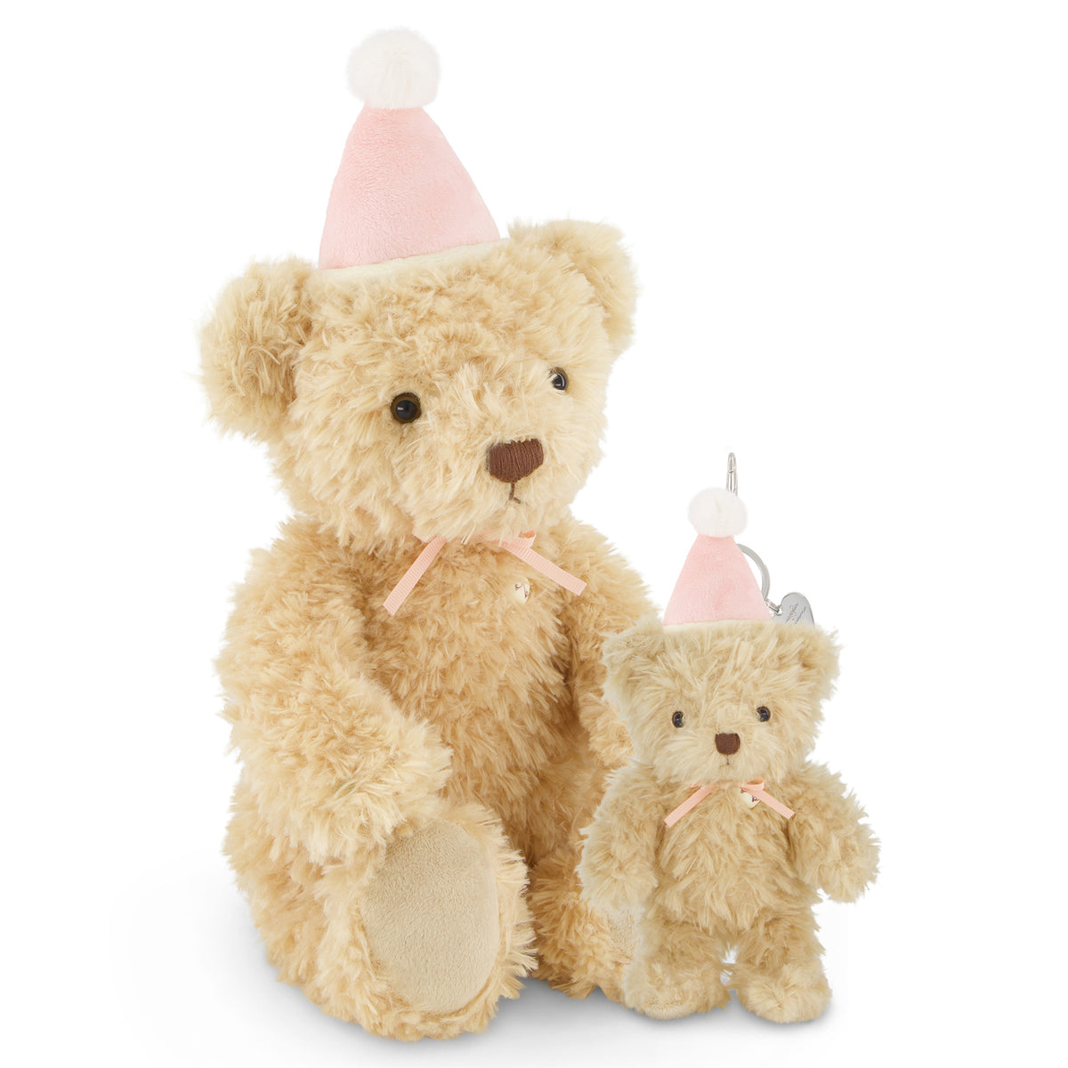 A beige teddy bear sits beside a smaller matching teddy bear ornament, both wearing pink party hats with white pom-poms and pink ribbons, on a white background.