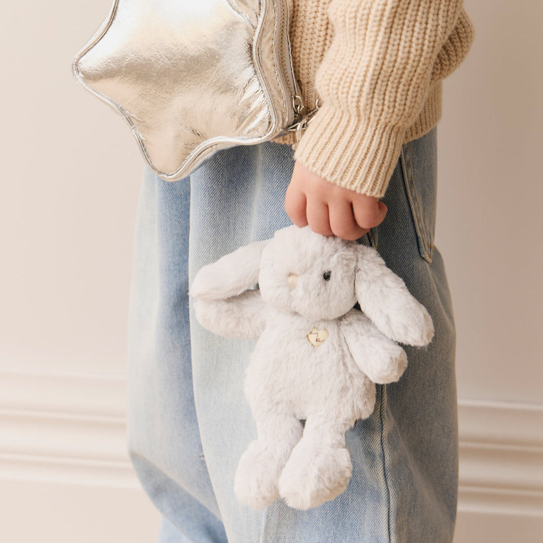 Child in jeans and a sweater holding a stuffed bunny and a silver star purse.
