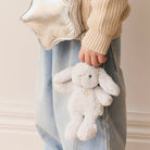 Child in jeans and a sweater holding a stuffed bunny and a silver star purse.
