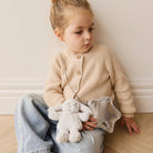 A young girl wearing a beige cardigan, jeans, and holding a plush bunny and silver star purse.