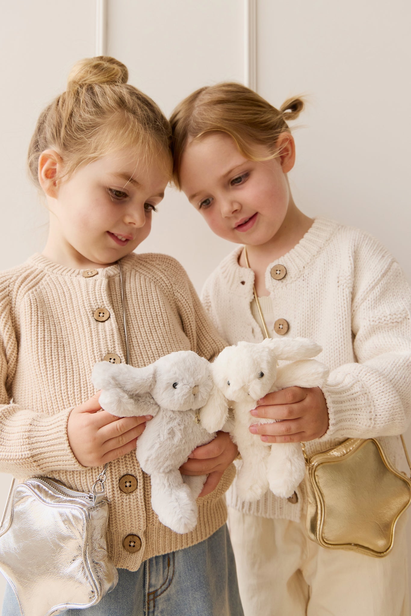 Two young girls in matching sweaters holding stuffed bunnies and wearing star-shaped purses.