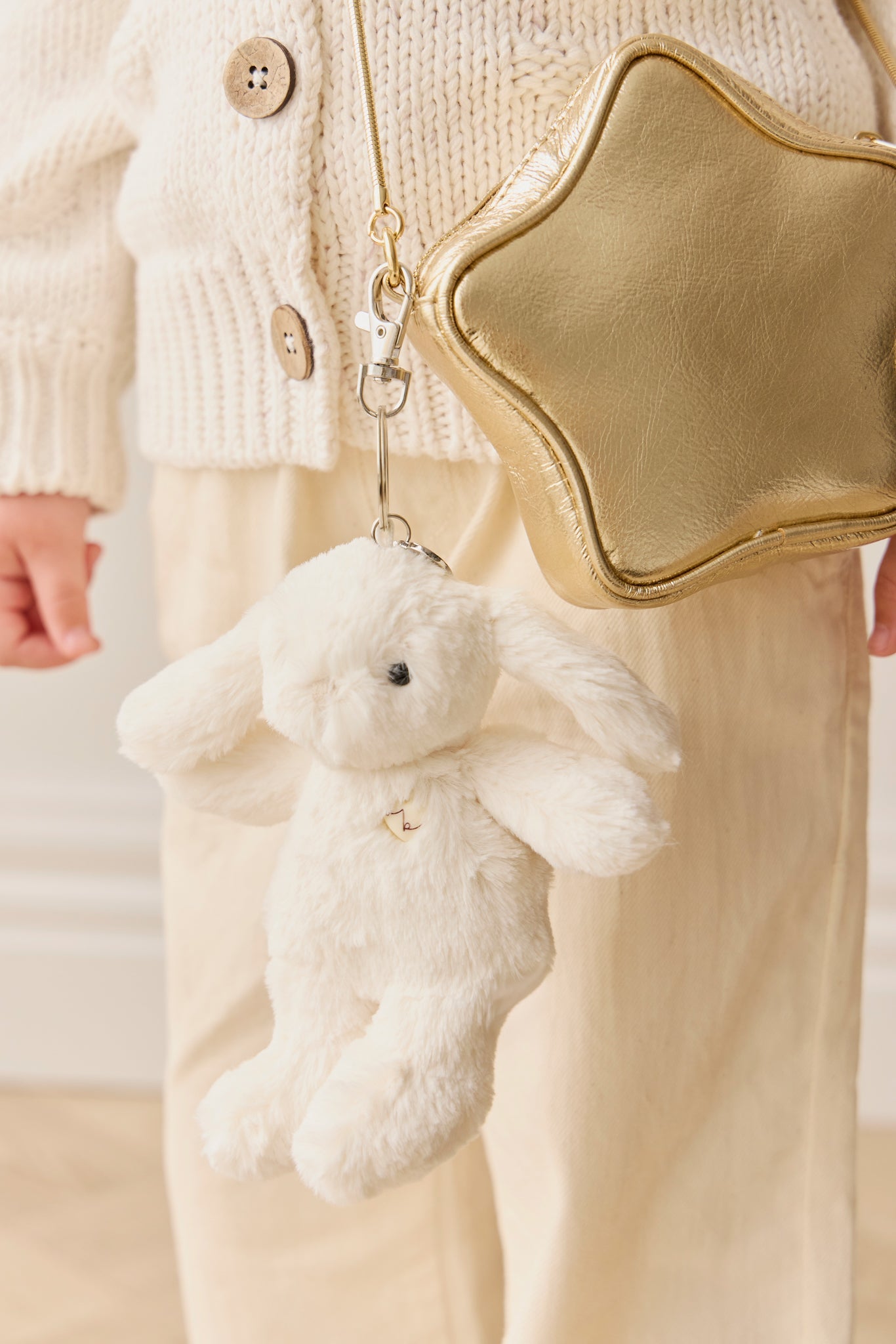Child wearing beige knit sweater, holding gold star purse with white bunny keychain.
