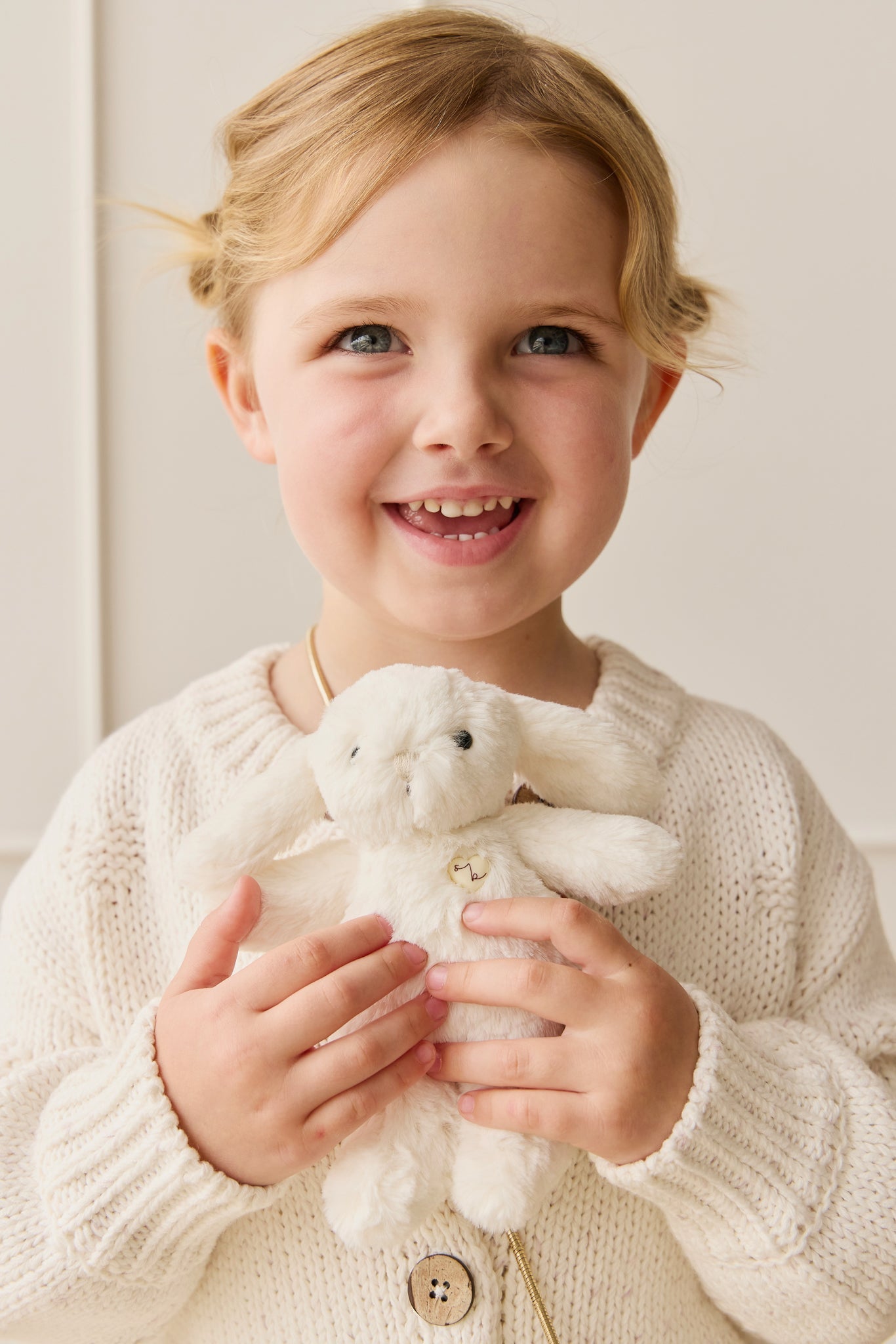 Girl holding a stuffed white bunny in a cream sweater.