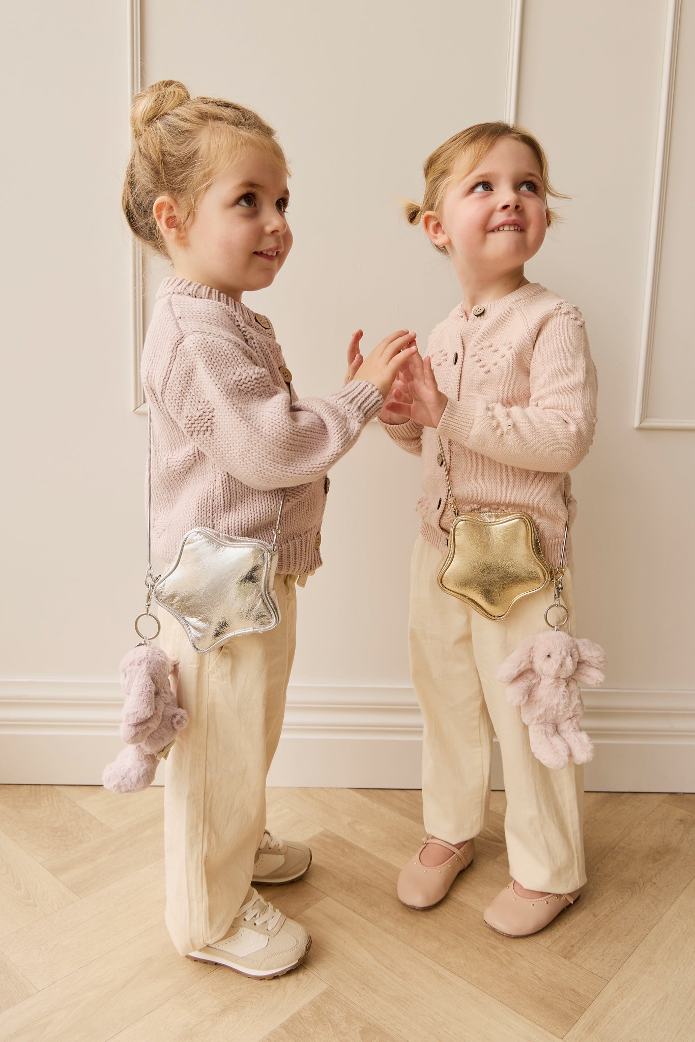 Two young girls, light pink sweaters, star-shaped purses, standing indoors.