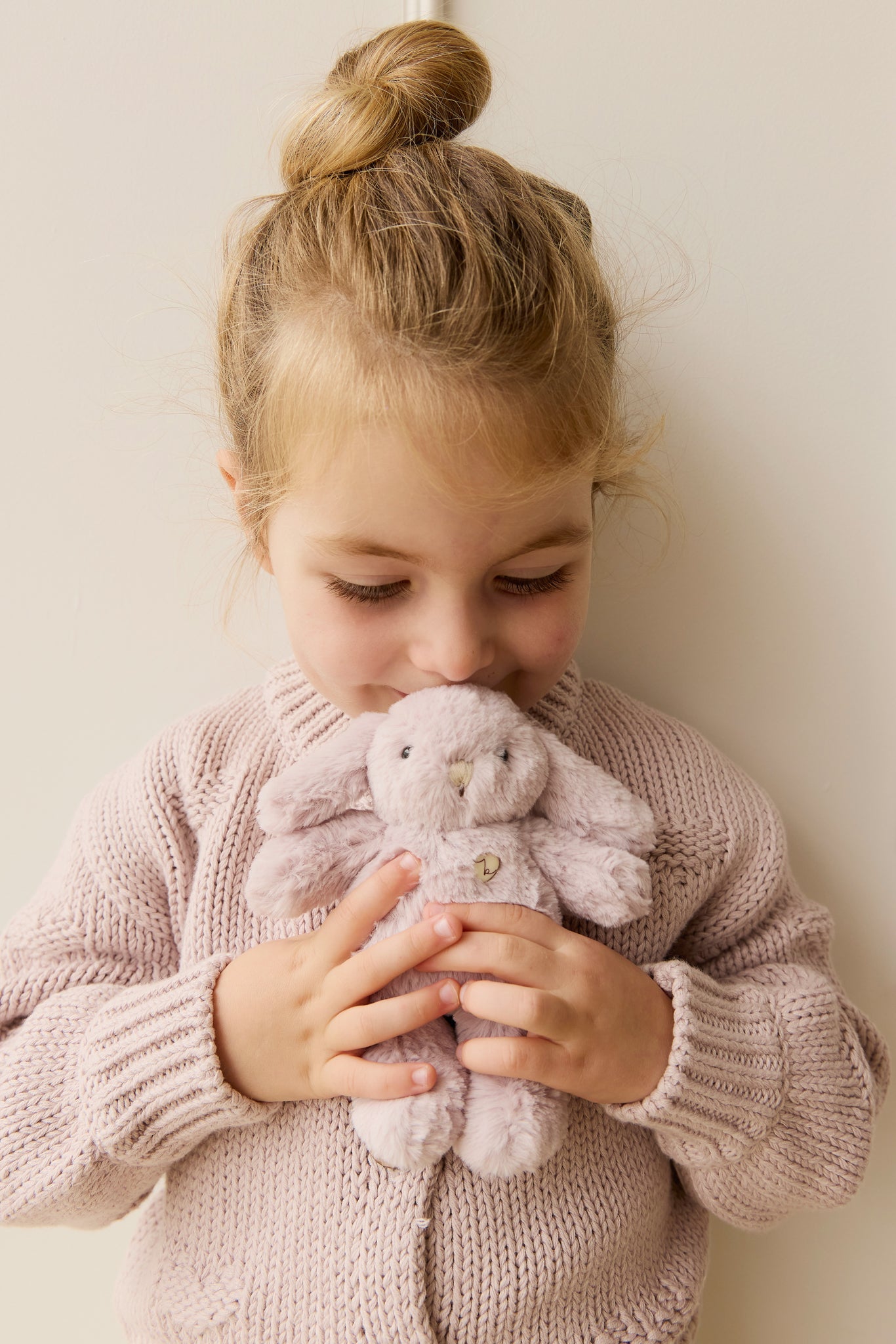 Girl holding a plush rabbit, wearing a pink knitted cardigan.
